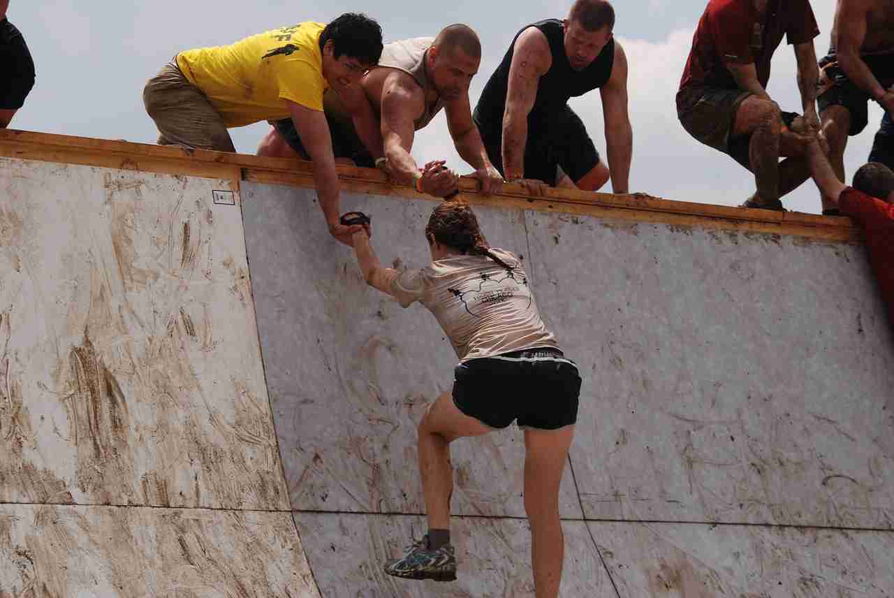 The goal of training is to build resilience athlete assisted up wall by team in obstacle course